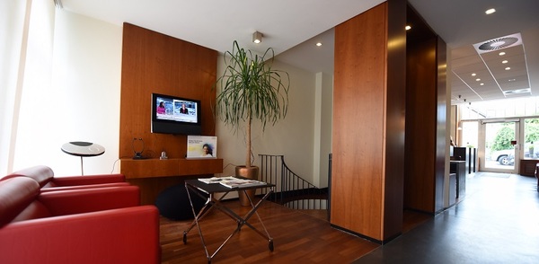 Modernes Wartezimmer mit roten Ledersesseln, Holzdekor, TV und heller Empfangsbereich.